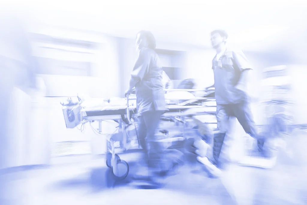 Login to xLocums and connect with locum tenens ER teams in action, rapidly pushing a stretcher in a hospital corridor with motion blur.