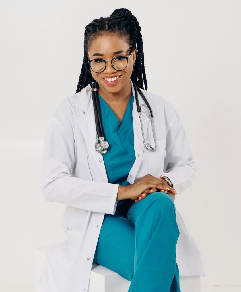 Physician Assistant Jobs with xLocums: Female physician assistant in a lab coat and scrubs, smiling at the camera with hands on her thigh.